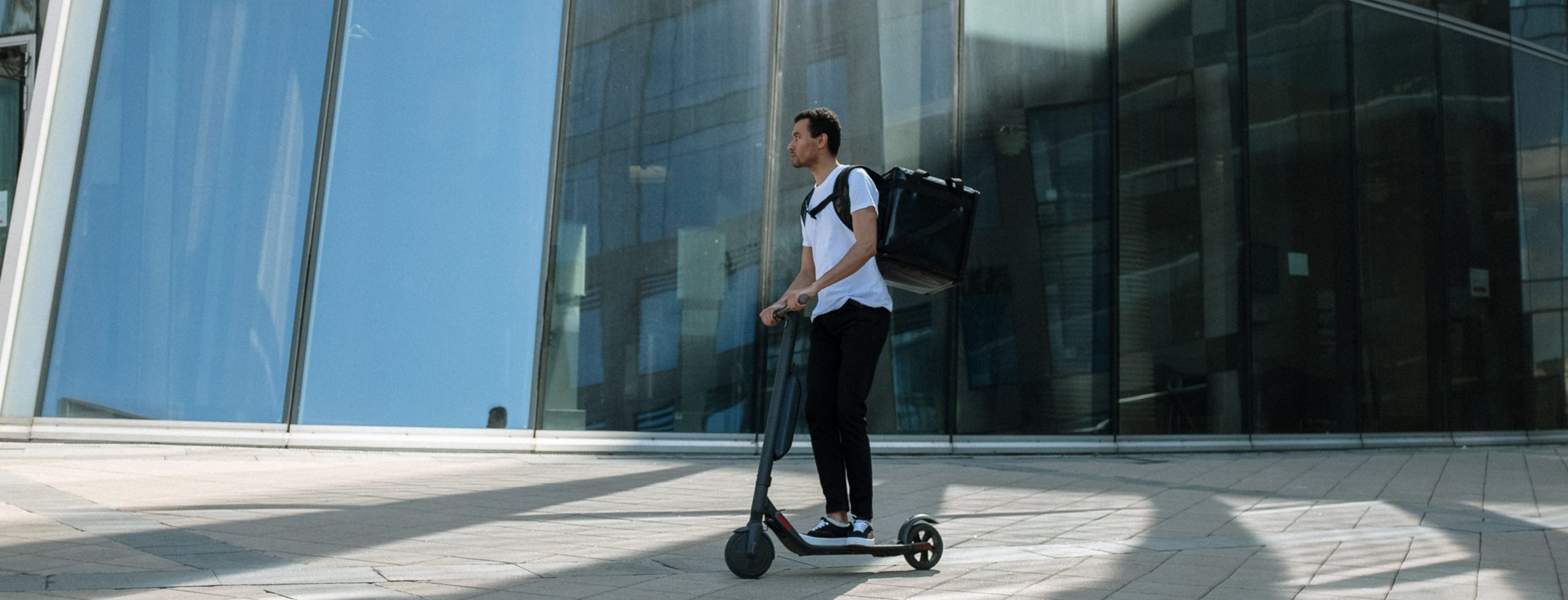 person on scooter wearing backpack in front of glass building