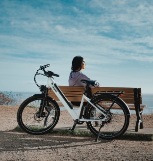 person sitting on bench by ocean with electric bike leaning against bench